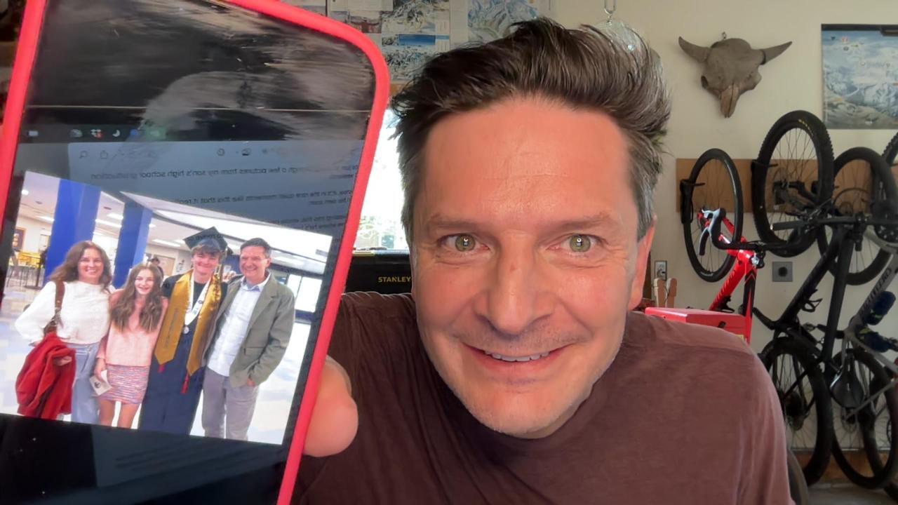 Robb holding up a phone with image of his family on son's graduation